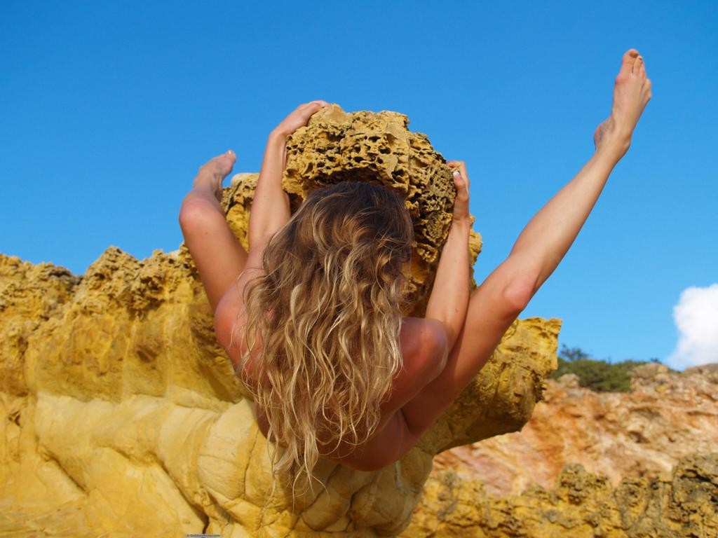 Honey blonde is tanned and naked in golden rocky desert while posing flexibly