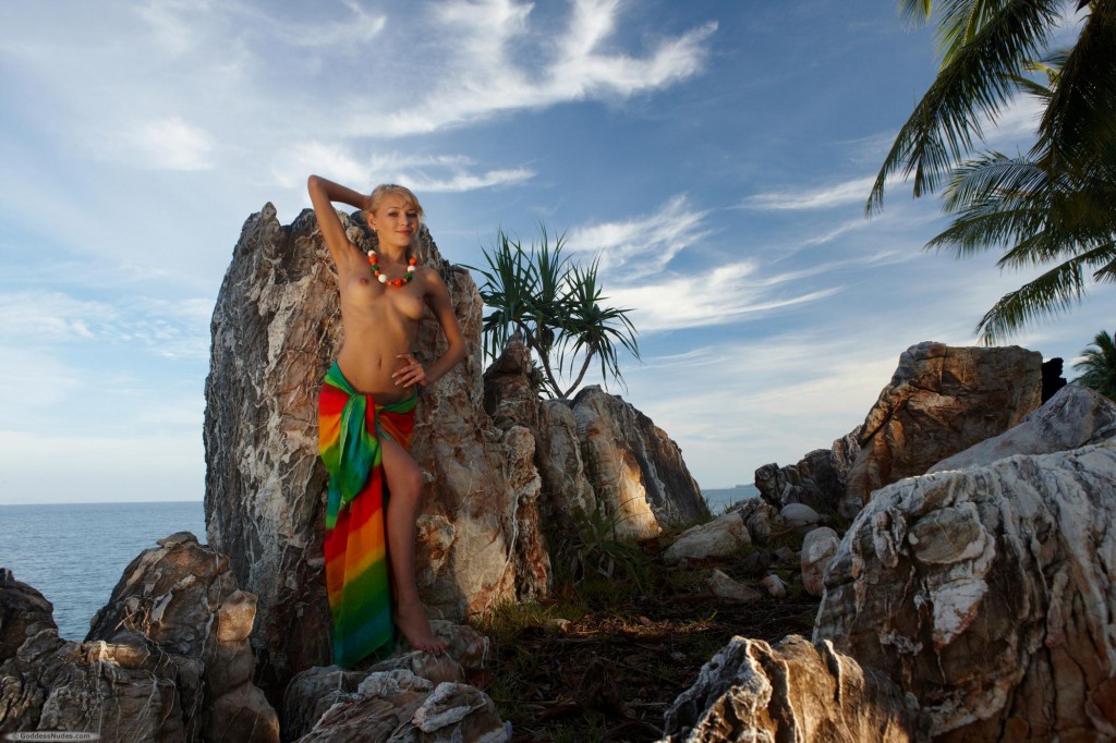 Model swishes bright fabric around her nude and sleek body on tropical rocky beach